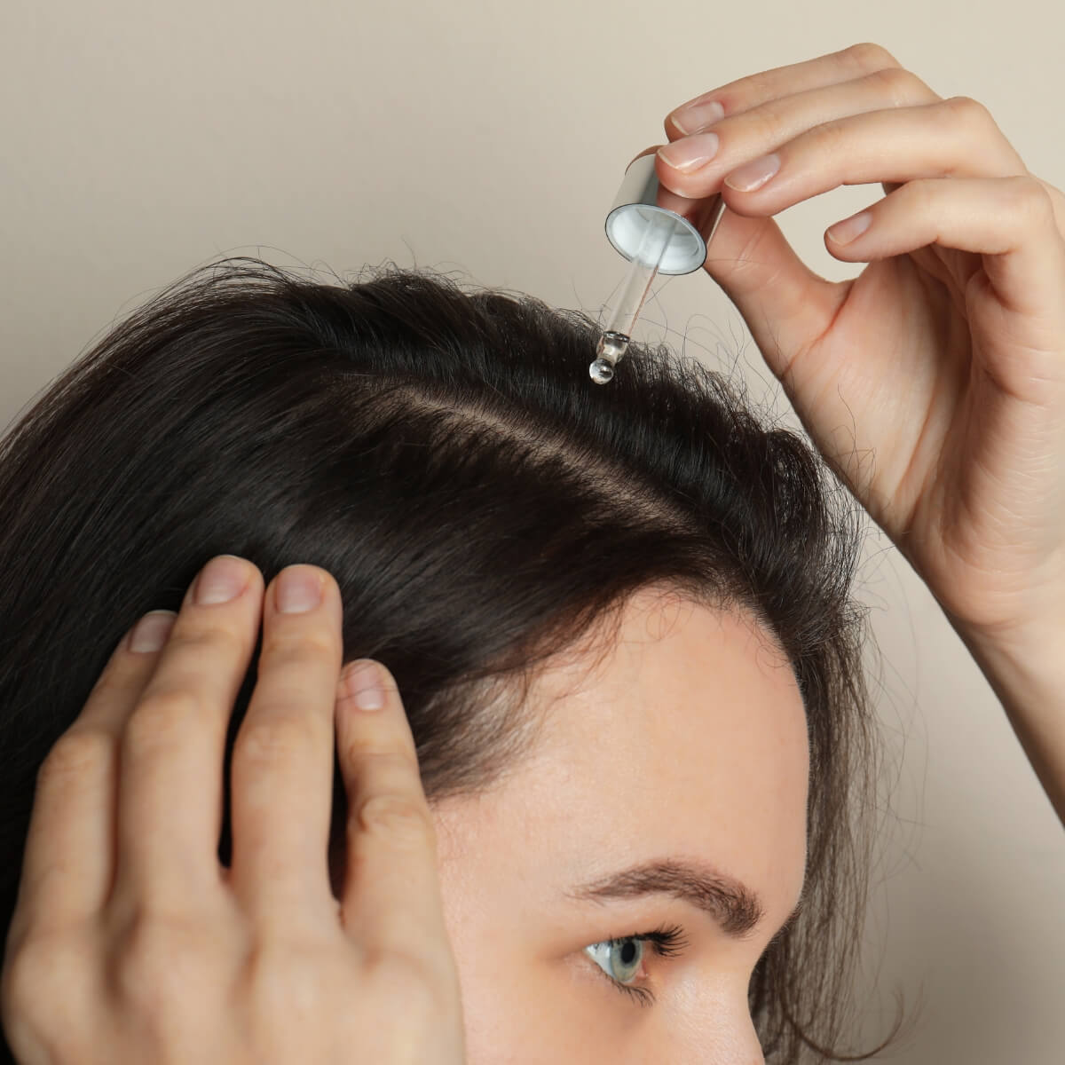 Woman dropping hair oil into her parted hair