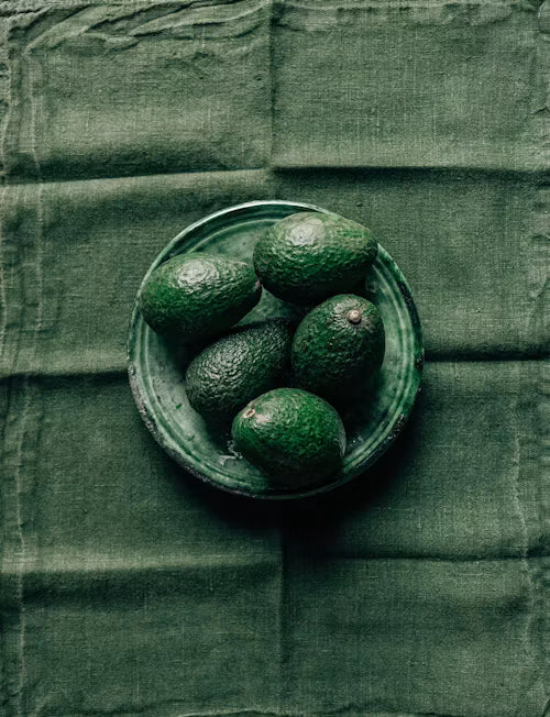 Green avocados in a bowl on a green textured fabric background