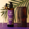 Saabuni Jasmine hair oil with a dropper and wooden comb on a purple surface with green leaves in the background