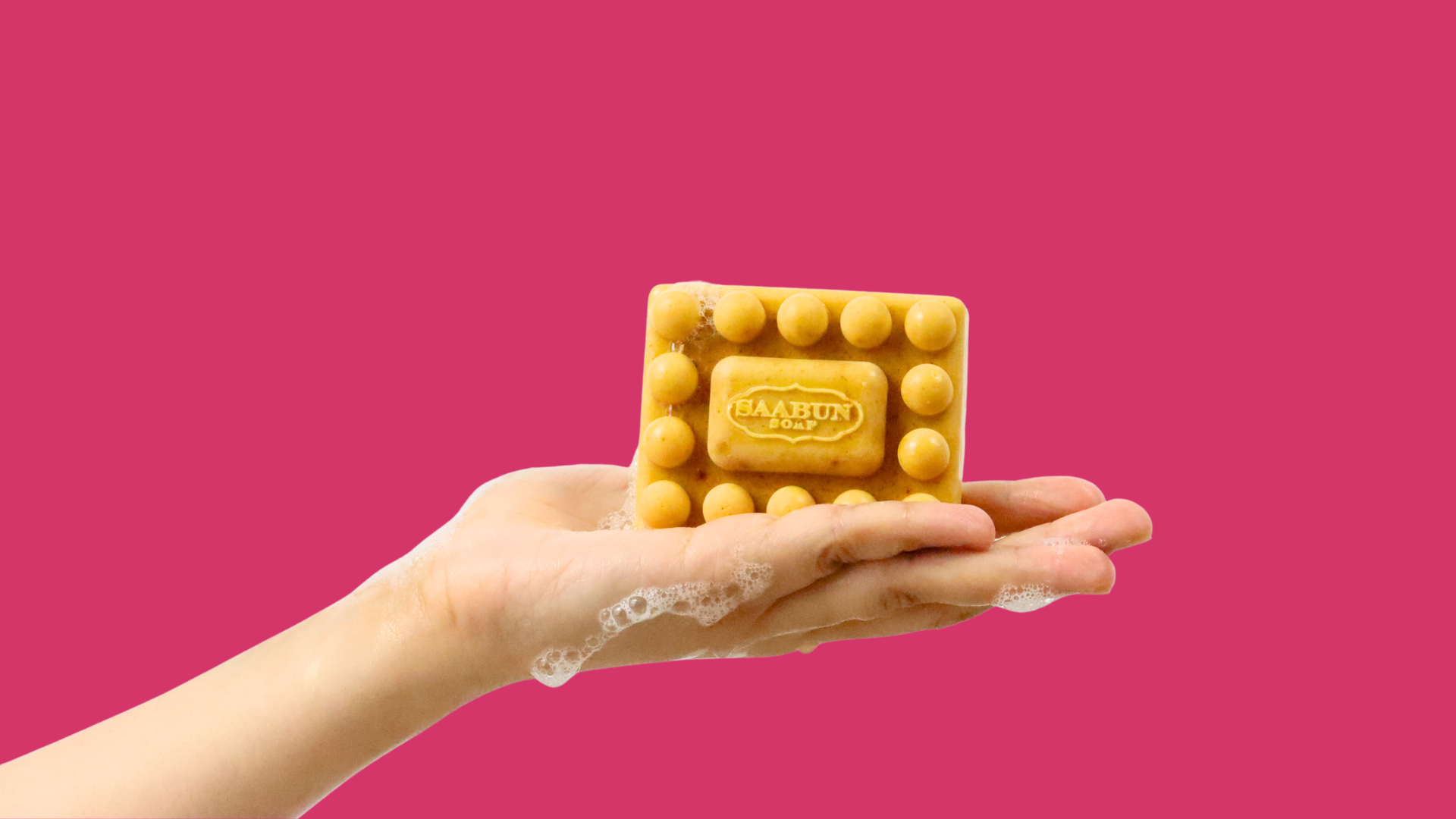 Hand holding a massaging soap bar on a pink background