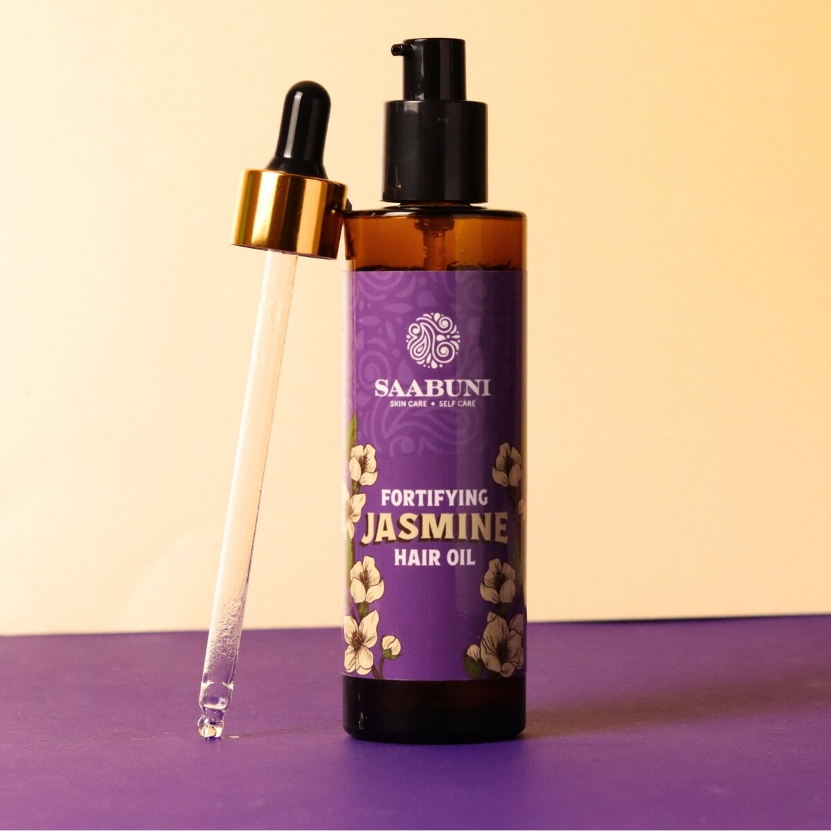 Saabuni Jasmine hair oil bottle with dropper on a purple surface and beige background