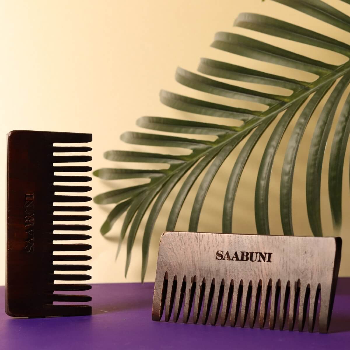 Two combs, both brown, with 'SAABUNI' branding, on a purple surface with a leafy background.