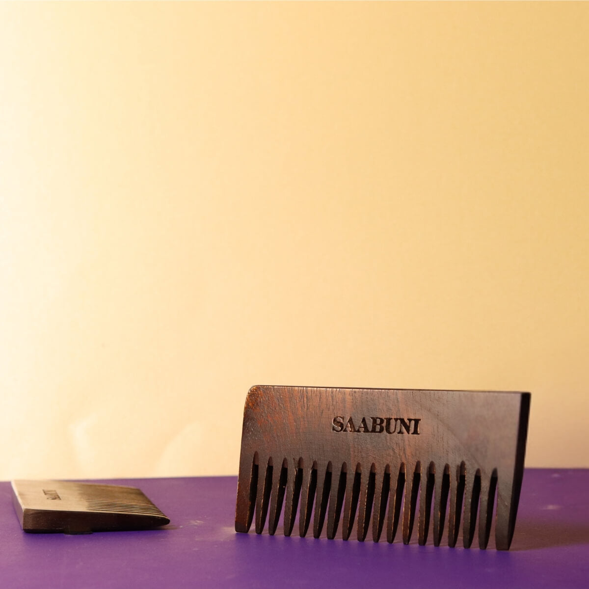 Wooden comb with 'SAABUNI' branding on a purple surface against a beige background
