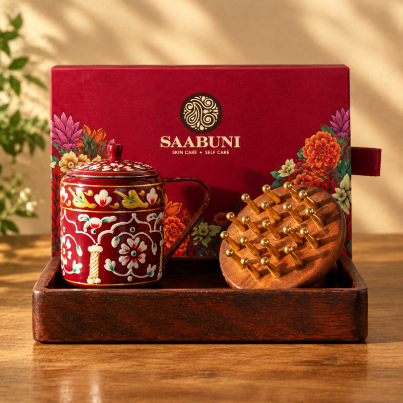 SAABUNI gift set displayed in a wooden tray, featuring a red floral-patterned mug with a lid, a wooden scalp massager with brass tines, and the red branded gift box behind it.