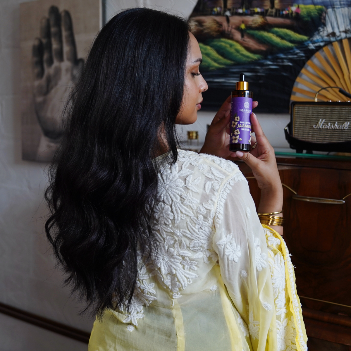 Woman holding a bottle of hair care product in a room with wall art and a Marshall amplifier.