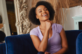 female model smiles in blue chair wearing a lilac top