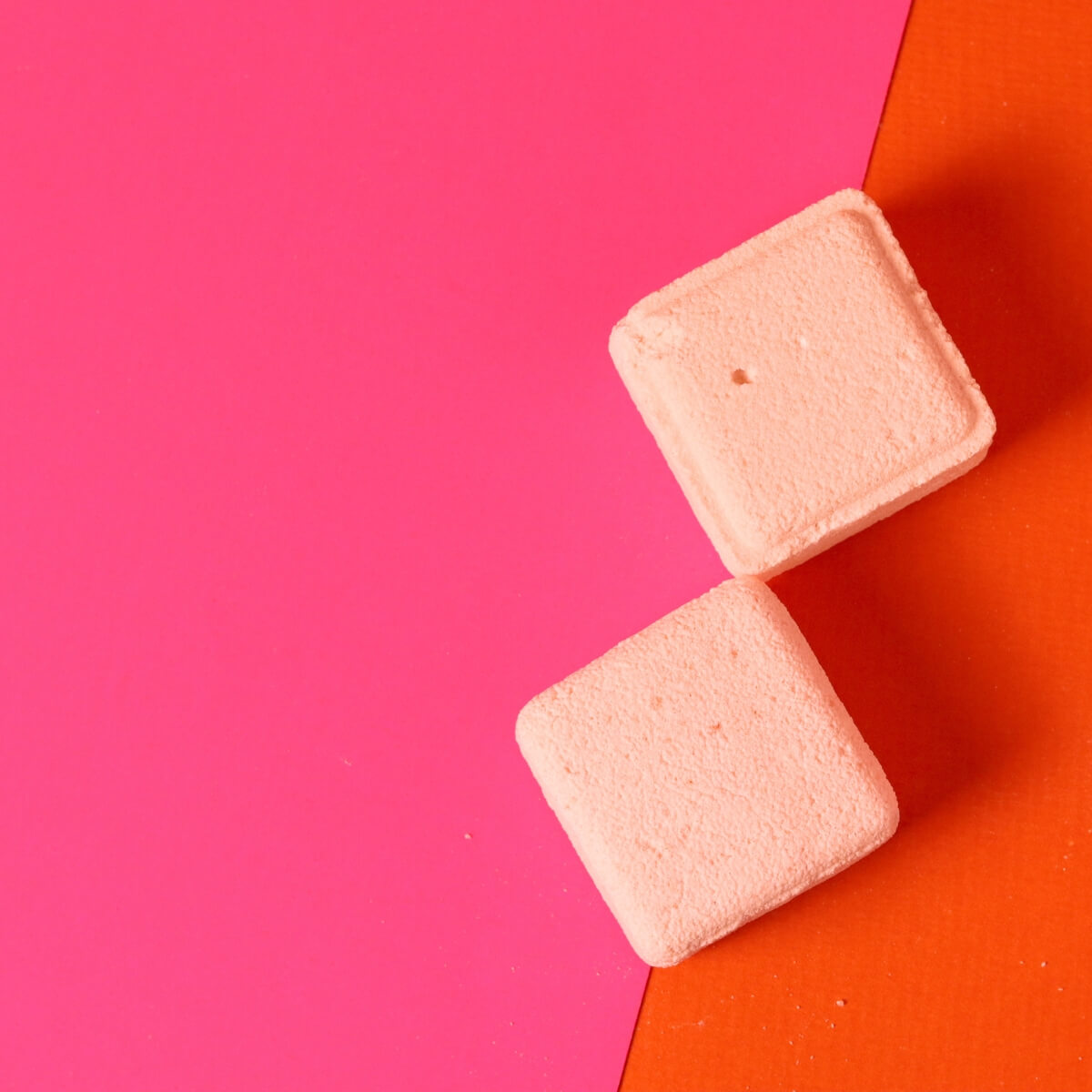 Two pink square shower melts on a pink and orange background